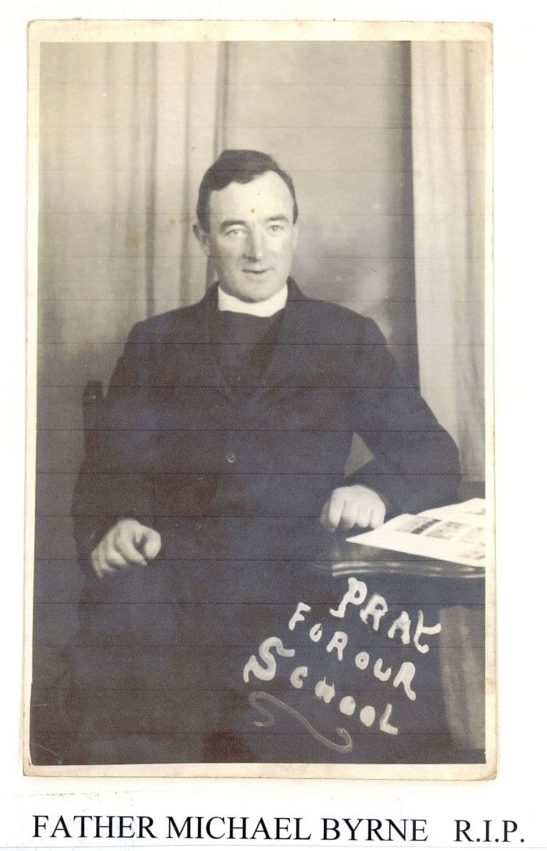 A studio portrait of a priest in a dark suit and clerical collar, seated with one hand on a table; “Pray for our school” is written in white across the lower part of the print, and a label below reads “Father Michael Byrne R.I.P.”