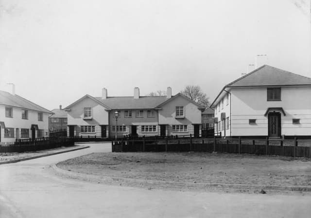 A short close of new white rendered houses with hipped roofs around a turning space, the verges still bare earth.