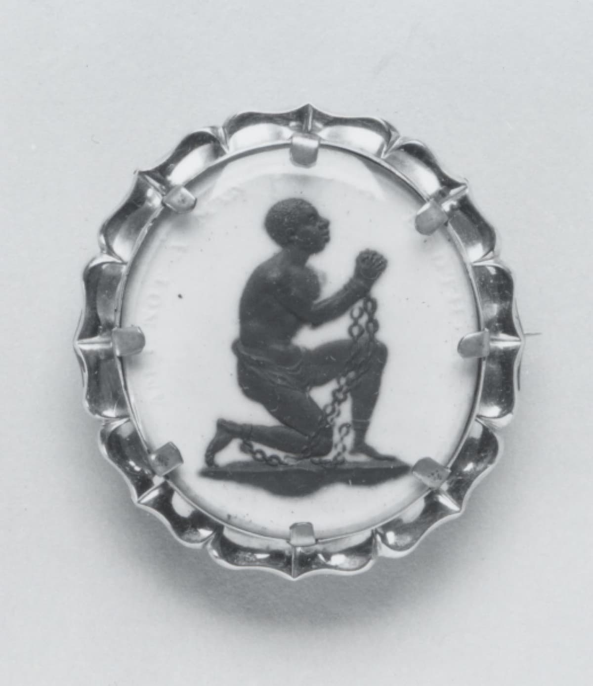 Oval white ceramic medallion showing a kneeling black figure in chains, with the words Am I Not a Man and a Brother.