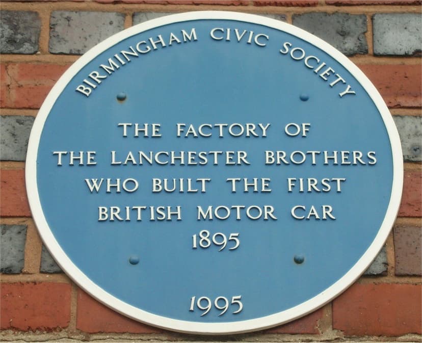 Oval blue Birmingham Civic Society plaque on banded red and blue brickwork, reading The factory of the Lanchester brothers who built the first British motor car 1895, dated 1995.