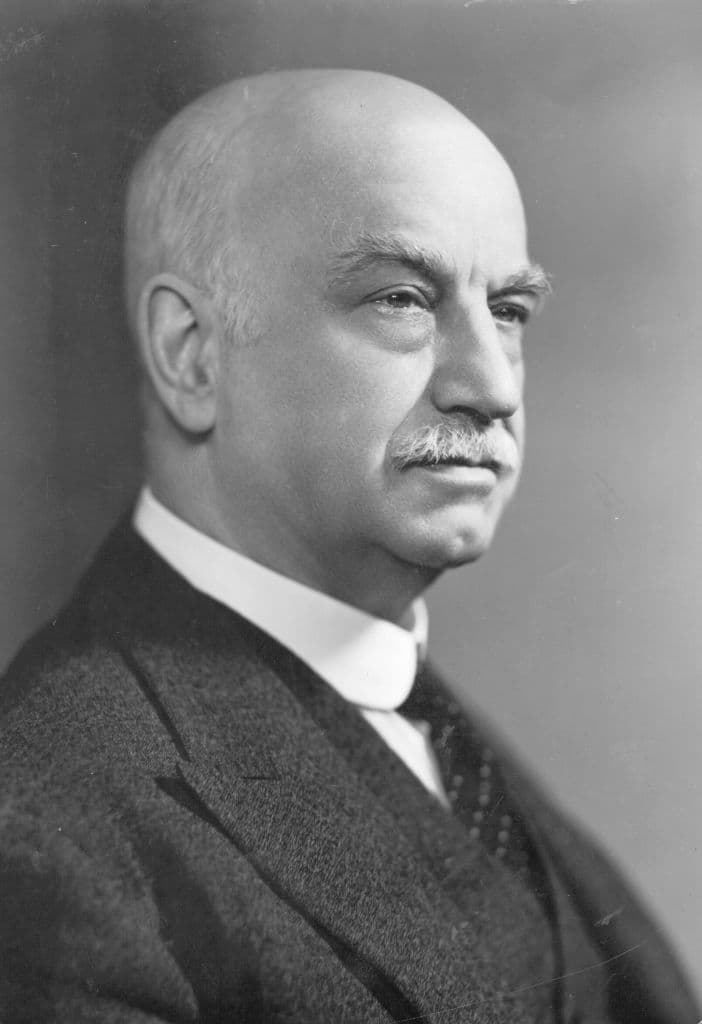 Black-and-white portrait photograph of Herbert Austin in later life, bald, with a grey moustache, in a dark suit.