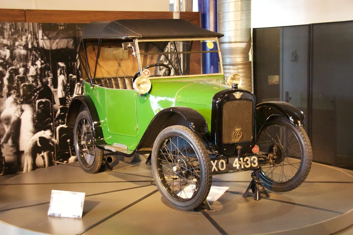 A small green 1920s car with its black hood up, registration XO 4133, on a museum display stand.