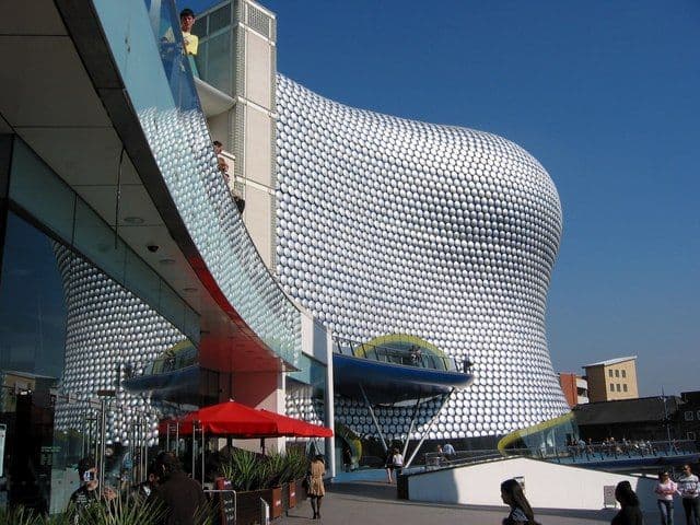Curved building covered in shiny metal discs on a blue background.