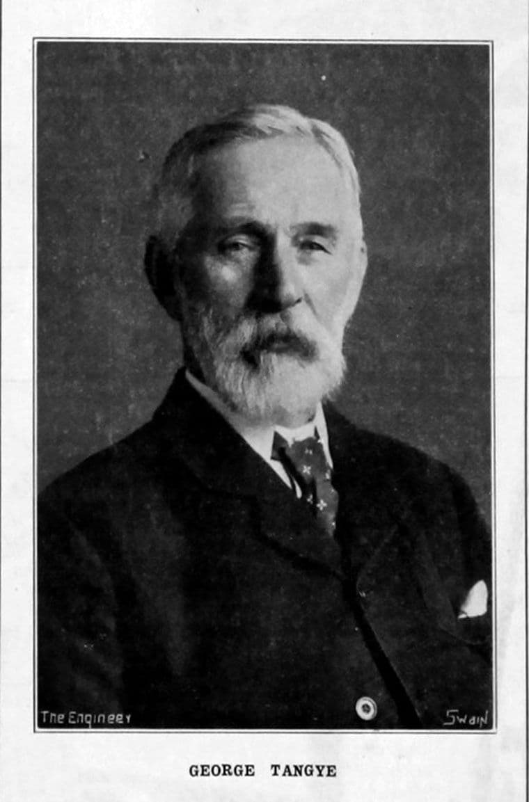 Black-and-white portrait of an elderly man with white hair and a full white beard, in a dark suit and patterned tie.