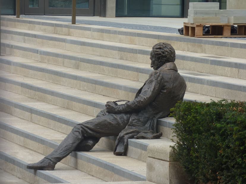 A bronze figure reclining on wide new pale stone steps, with modern buildings behind.