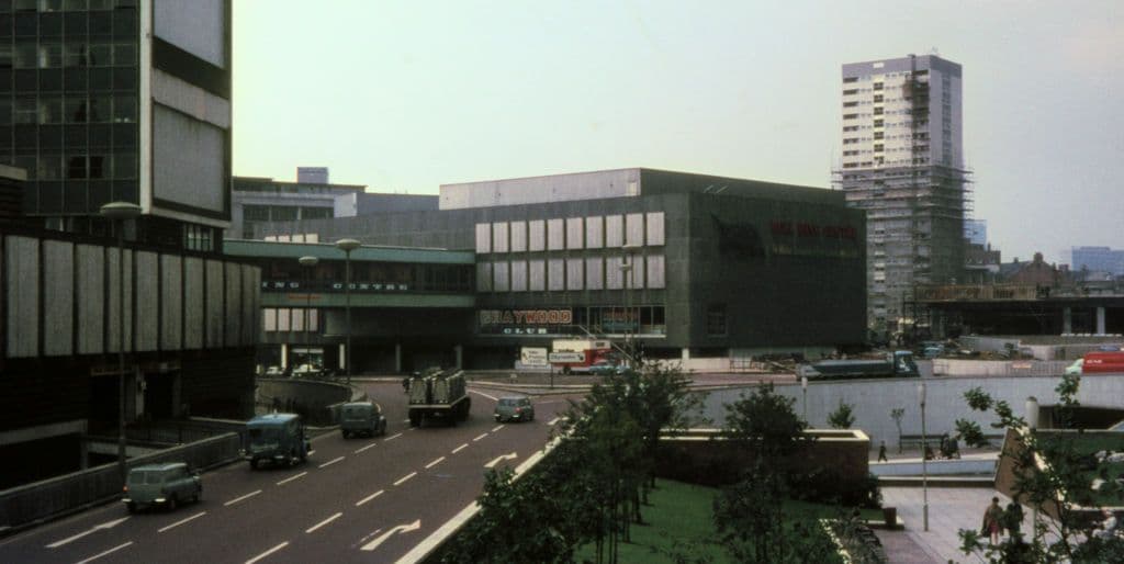 A small public garden beside a busy road junction, with a station under construction behind.