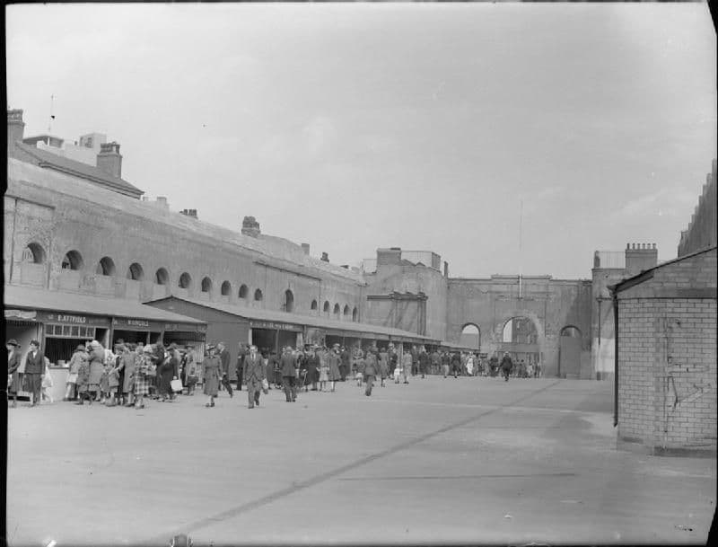 Shoppers among stalls inside a roofless hall.