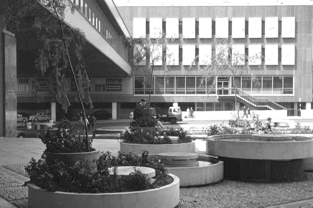 A raised concrete walkway between new modern buildings, with round concrete planters below.