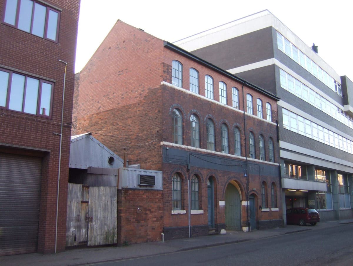 A row of brick workshop buildings with many windows along a street.