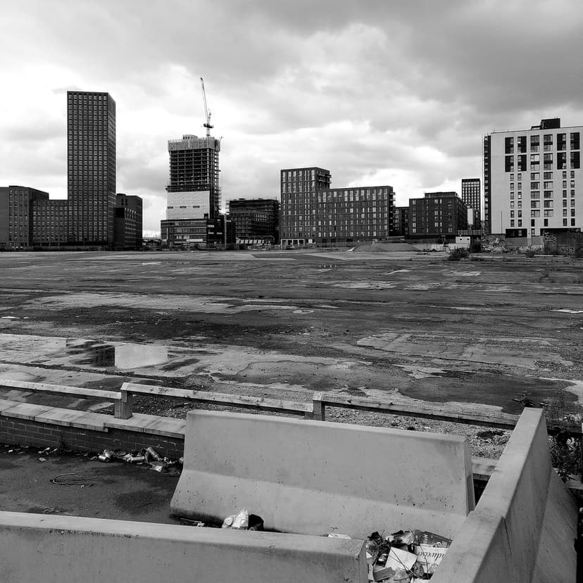 A cleared and fenced city-centre site seen from a street, with buildings beyond.