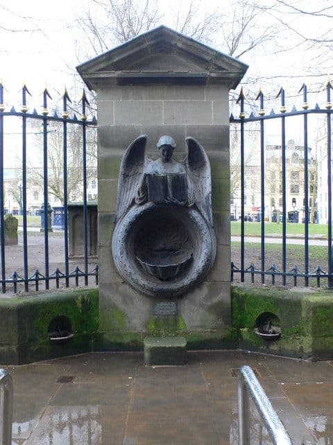 A stone drinking fountain with a carved angel holding an open book above a shell basin.