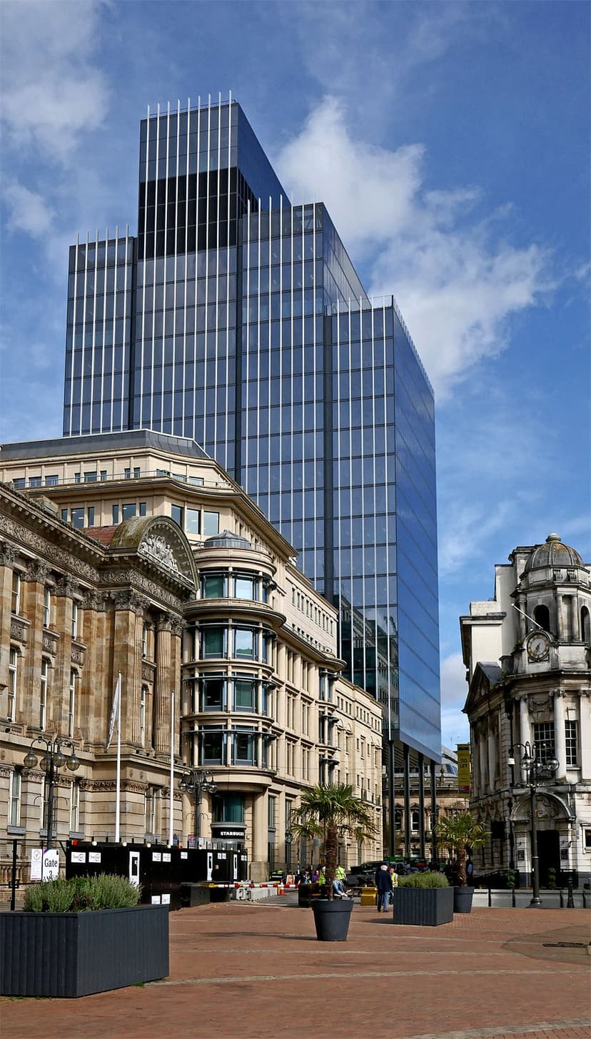 A paved city square rising towards a street of Victorian buildings.