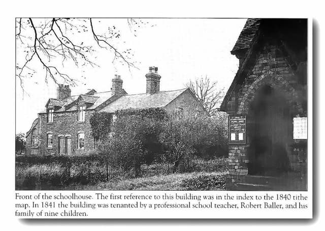 An old ivy-covered brick schoolhouse with dormers and tall chimneys behind a hedge, with a church noticeboard in a brick porch at right