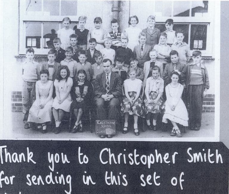A school-archive page: a class of about thirty-five children in four rows with a male teacher seated in the centre in front of the school windows; a slate reads “Kingsthorne School Class …”. Below, a blackboard panel reads “Thank you to Christopher Smith for sending in this set of …”.