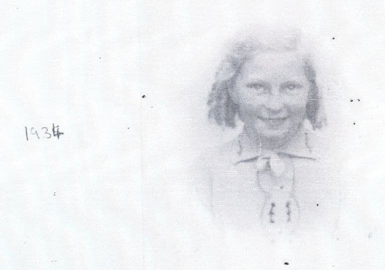 A very faded photocopy of a head-and-shoulders portrait of a young girl with shoulder-length hair and a collared blouse, with “1934” handwritten to the left.