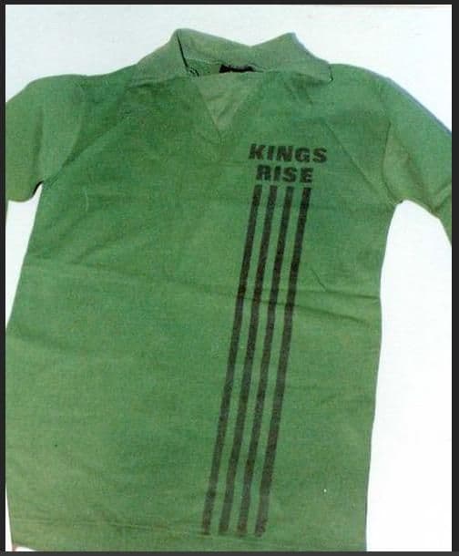 Colour photograph of a green long-sleeved collared sports shirt with “KINGS RISE” and four vertical black stripes printed on the front.