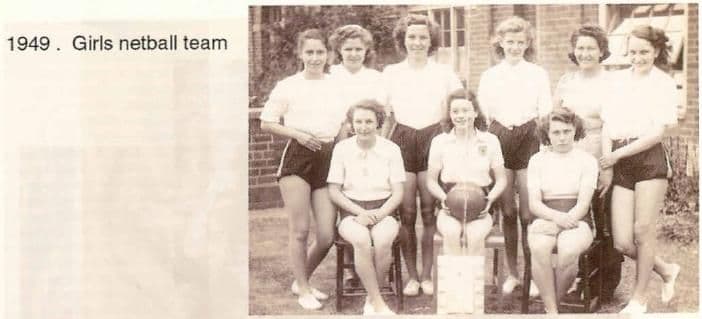 A scanned booklet page: nine girls in white blouses and dark shorts, three seated in front with a netball, outside a brick building. Printed beside it: “1949. Girls netball team”.