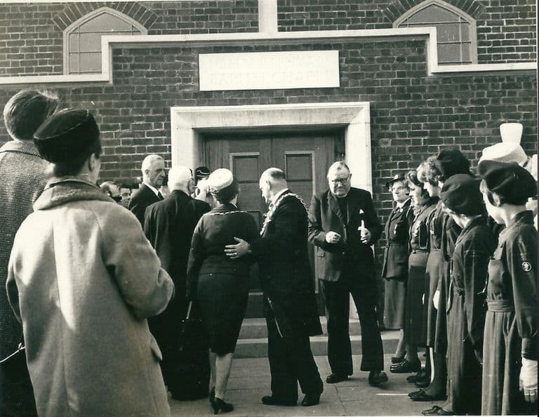 Black-and-white photo of a crowd at the door of a brick chapel inscribed “John Bunyan Baptist Chapel”: a man wearing a chain of office and a woman in a hat stand with a minister, watched by uniformed girls in berets lined up on the right.