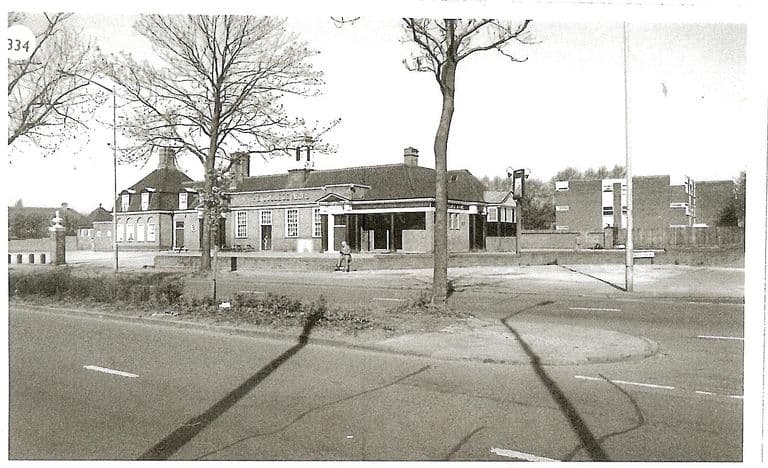 A book-plate photograph of the College Arms seen across a wide road with a planted central reservation and bare trees: a long brick pub with dormer windows, a pillared porch and a hanging sign, with flats on the right. The number “334” is printed in the top corner.