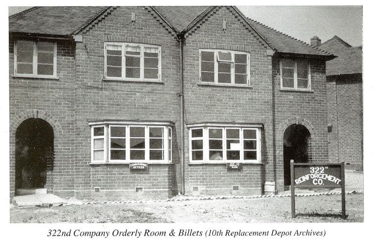 A scan of a book page: a pair of brick semi-detached houses with arched porches and bay windows, small signs reading “Commanding Officer” in the windows and a board in front reading “322nd Reinforcement Co.”. The printed caption reads “322nd Company Orderly Room & Billets (10th Replacement Depot Archives)”.