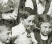 A very small crop from an old school group photograph showing a boy with short hair in a white shirt and tie.