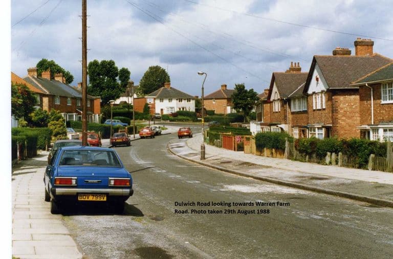 Colour photo of Dulwich Road curving away between brick semi-detached houses with front hedges and fences, a blue Datsun saloon parked in the foreground and other cars further along; a caption is printed on the image.