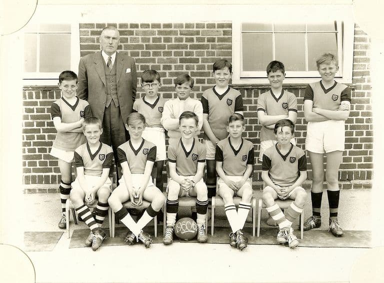 School football team of eleven boys in dark shirts with light collars and striped socks, with an older man in a three-piece suit; the ball is marked “1960-61”.