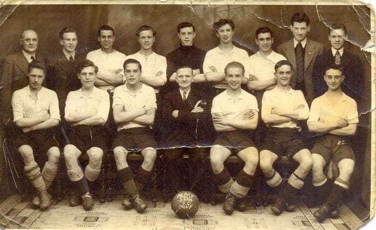 A creased sepia studio photo of a football team in light shirts and dark shorts, arms folded, with officials in suits; the ball in front is marked “Perry Star F.C. 1946-7”.