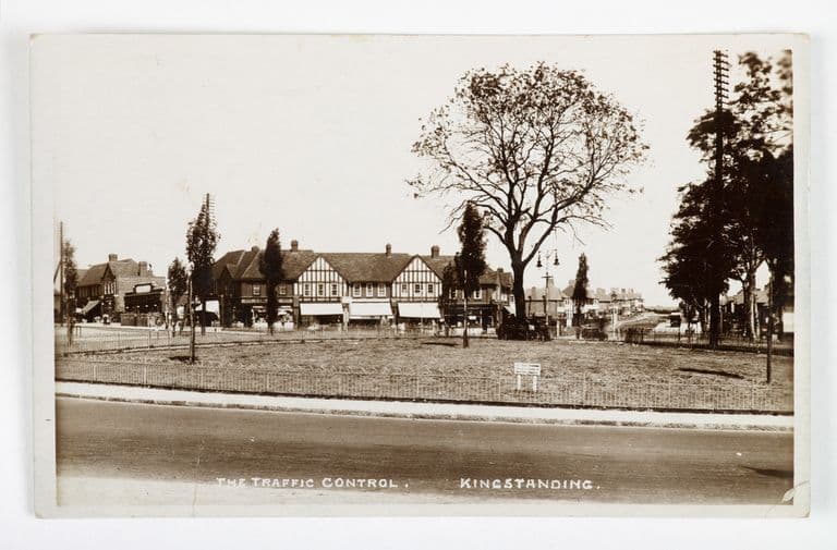 Sepia postcard titled The Traffic Control, Kingstanding: the railed garden in the middle of the Circle with the new shopping parade behind