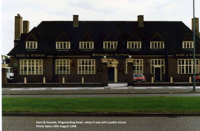 The long front of the Hare & Hounds pub with seven dormer windows, the names Hare & Hounds and Mitchells & Butlers in gold, and a grass verge in front