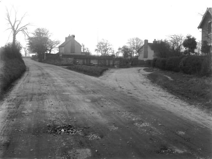 An unmade road forking in front of a cottage and outbuildings, with bare trees.
