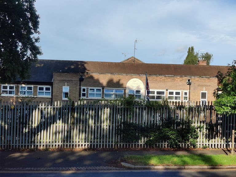 The Army Reserve Centre on Kingstanding Road seen from the road, with a white crest panel on the brick frontage behind palisade fencing.