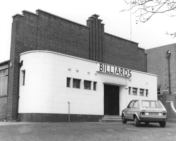 1984: A brick hall with a stepped parapet and a curved white rendered frontage bearing the word Billiards, with a car parked outside.