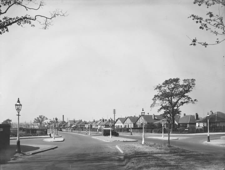 College Road at the Crossway Lane junction: a wide road with a traffic island, street lamps and rows of semi-detached houses.
