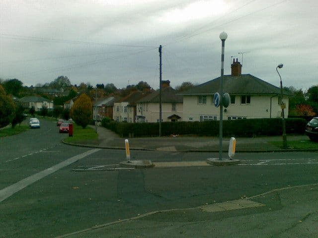 The junction where Hurlingham Road meets Danesbury Crescent, with a traffic island, street lamps and rendered houses around the curve.