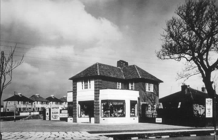 A detached corner shop with a double-height glazed shopfront and signs, with new houses behind.