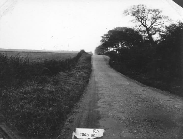 A narrow country lane rising between high hedges and fields, with a caption card reading Kings Road.