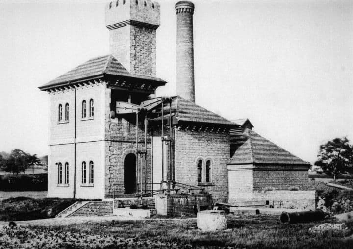 An Italianate brick pumping station with a tall square tower, arched windows and a separate chimney.