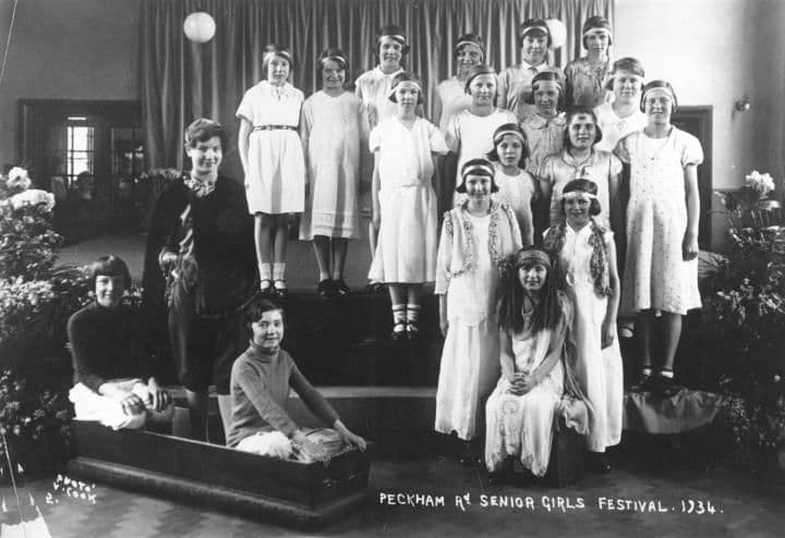 A group of girls in costume posed on a stage, captioned Peckham Rd Senior Girls Festival 1934.