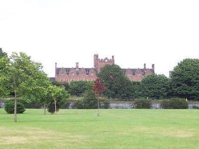 The turreted red-brick range of St Mary’s College, Oscott, seen above trees across a wide grass field.