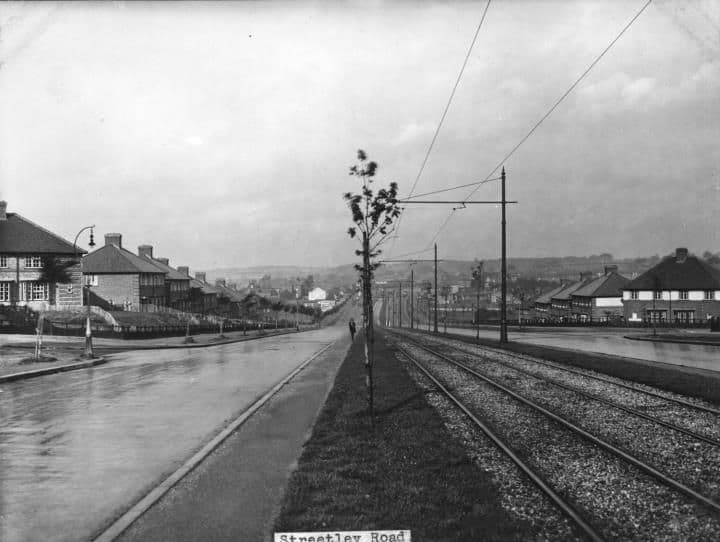 A wide road with a central tram reservation, overhead wires and young trees, lined with new houses; the print is captioned Streetley Road.
