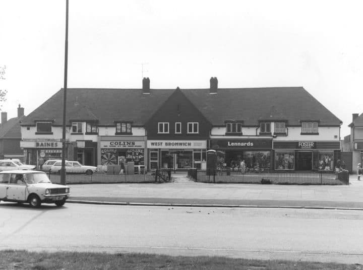 A parade of shops beneath a long tiled roof at the Circle, with shop signs including Baines and Lennards, and a parked car in front.