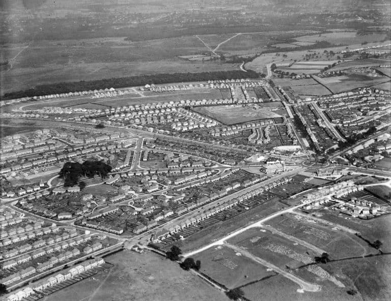 Oblique aerial photograph of the estate under construction around Bandywood Crescent: curving streets of new houses, a dark wooded clump and open fields beyond.