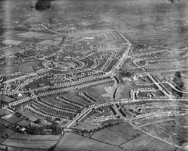 Oblique aerial photograph of the estate under construction: rows of new houses on curving and radiating streets, with fields in the distance.
