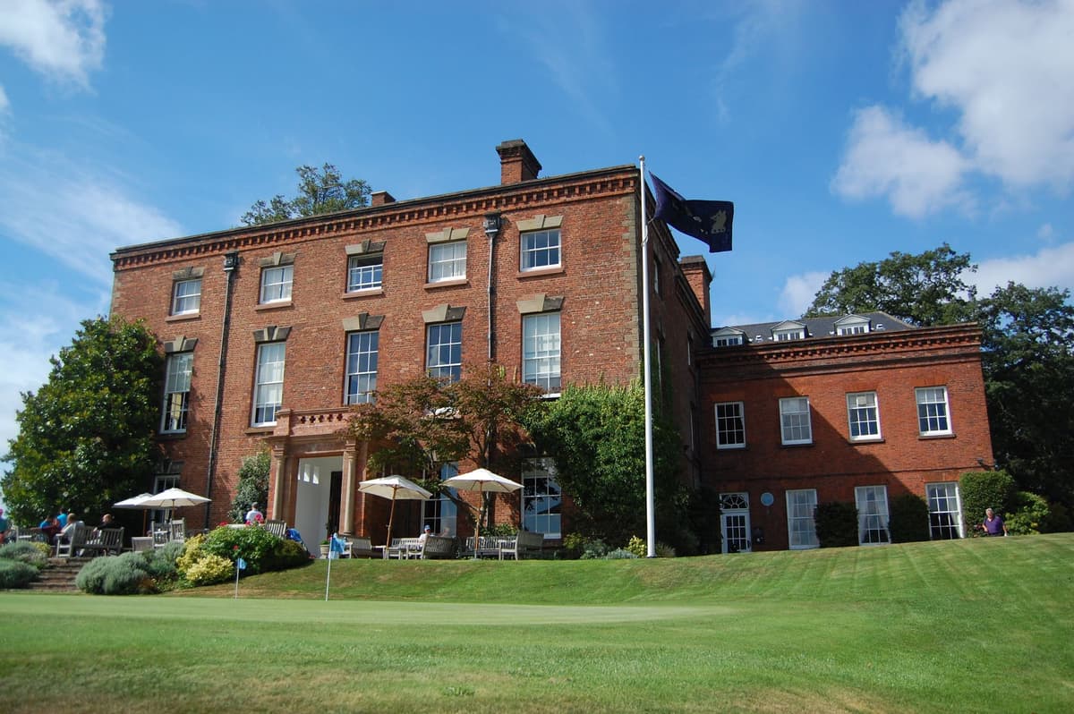 A red-brick Georgian house with white window frames, seen across a lawn.