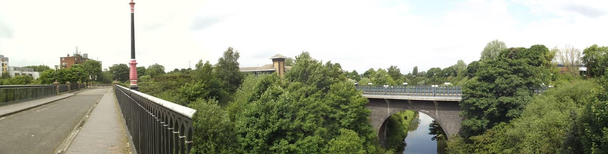 Panoramic view of a single-span cast-iron bridge over a deep canal cutting.