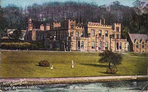 Painted postcard of a large battlemented Gothic-style house across a lawn and lake, with woods behind.