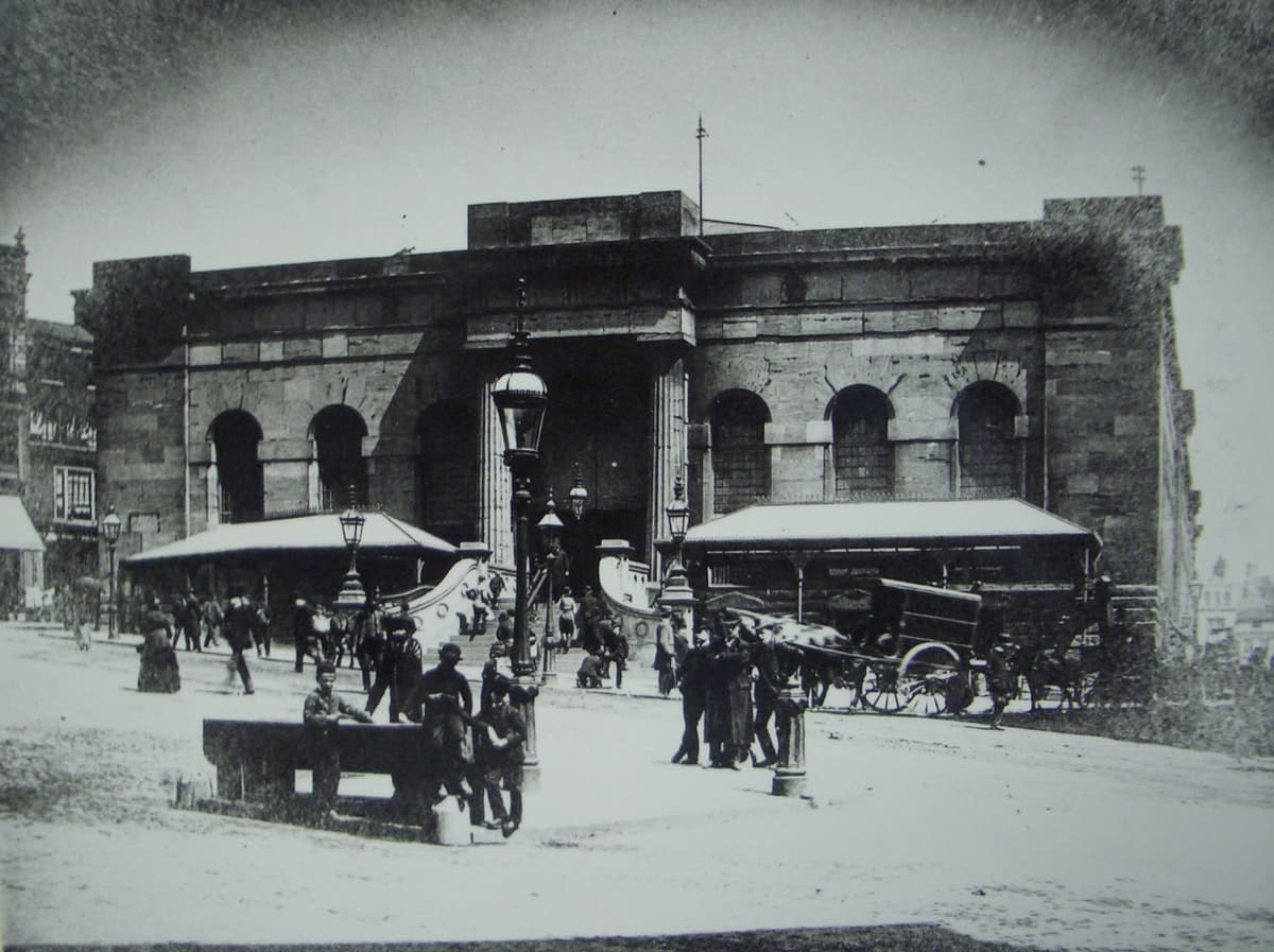 Old photograph of the west end of the Market Hall, with a broad flight of steps rising to the columned entrance on sloping ground.