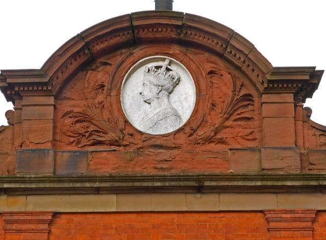 Terracotta medallion of Queen Victoria flanked by palm fronds on a brick wall.