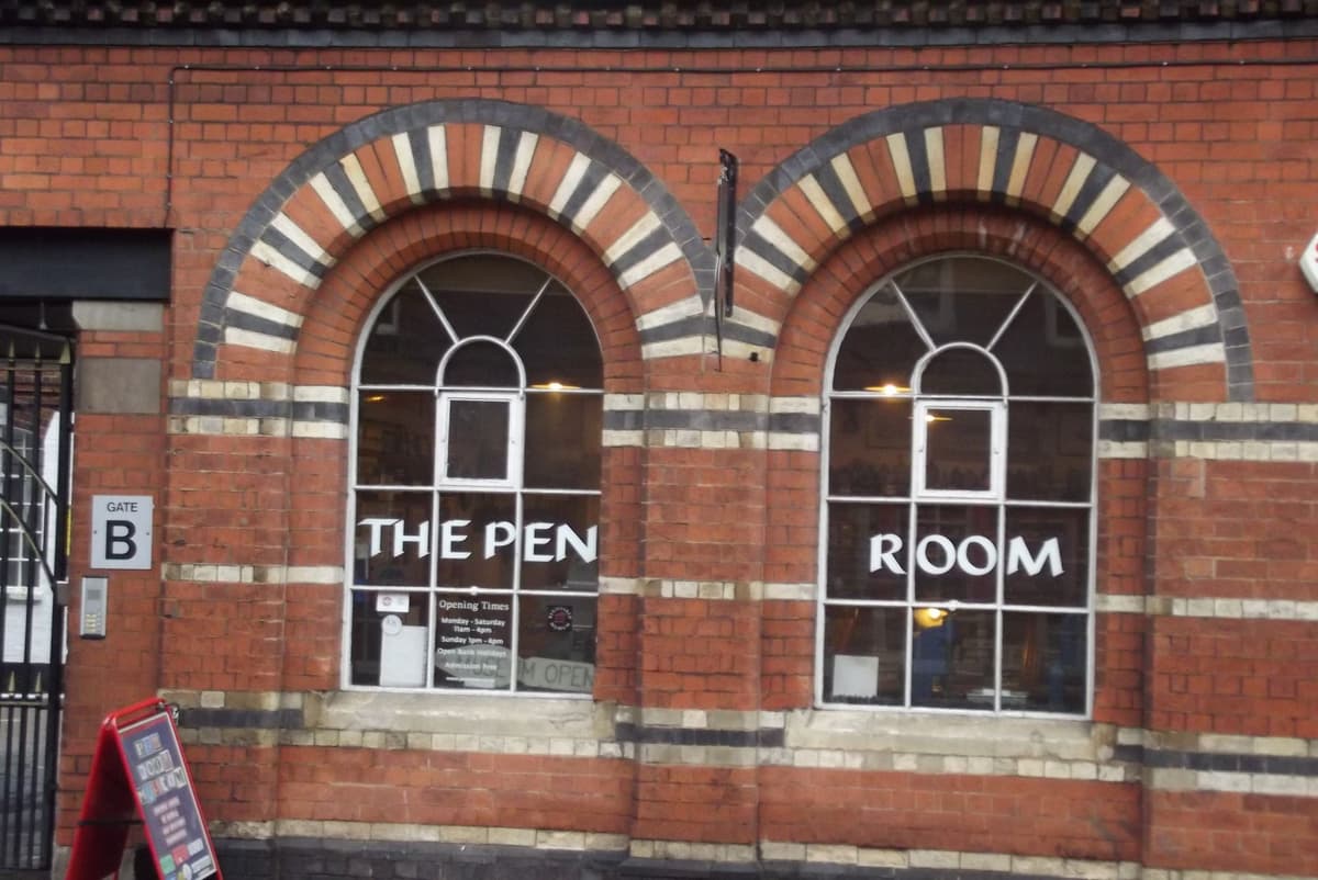 Arched windows in striped red and cream brick, lettered “The Pen Room”.